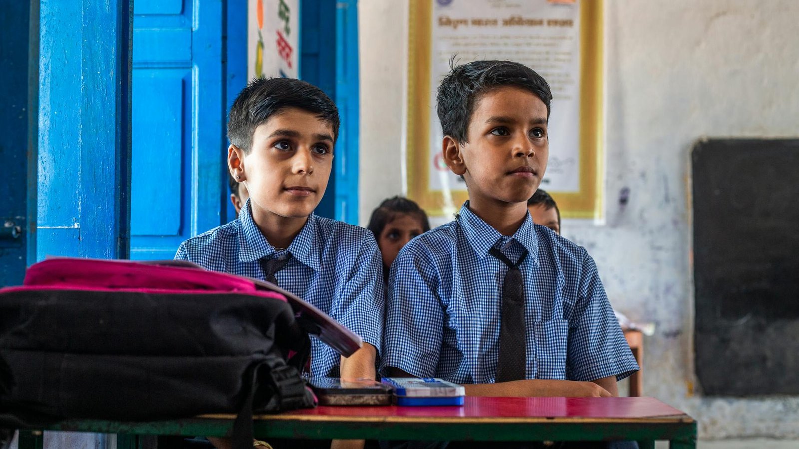 two boys in school uniforms sitting at desks
